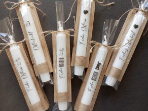 Weiße Kerzen mit Osterbotschaften in rustikaler Verpackung auf dunklem Hintergrund